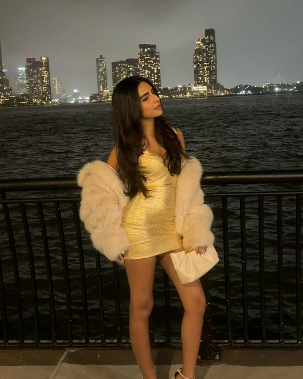 Siya Bhasin wearing the Casual Threat Naomi shimmery gold mini dress with a white jacket against the city skyline